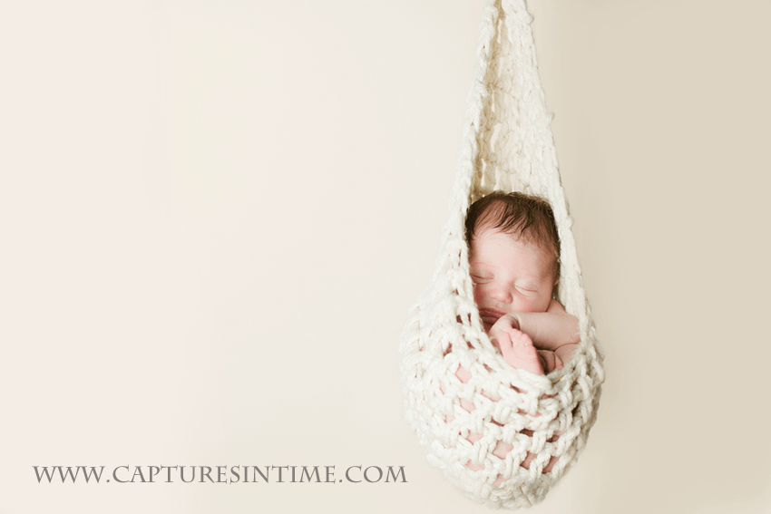 newborn hanging in hammock on cream