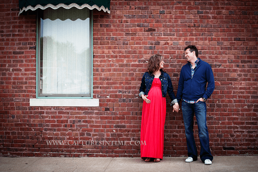 kansas city maternity session mom in red dress holding hands with dad looking at him