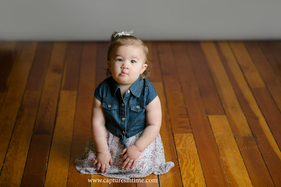 baby photography lees summit girl making funny face in denim and floral outfit on vintage floor