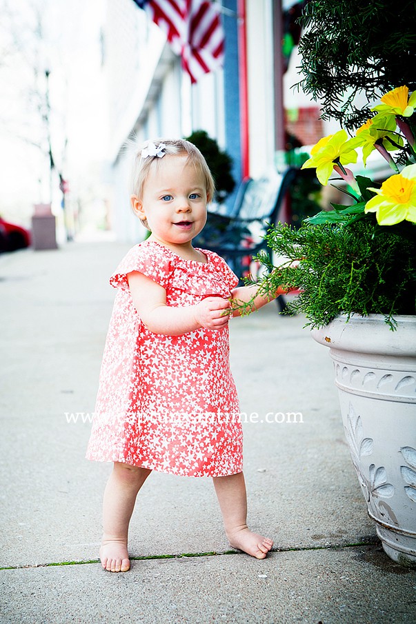 baby girl in orange dress outdoors by flowers