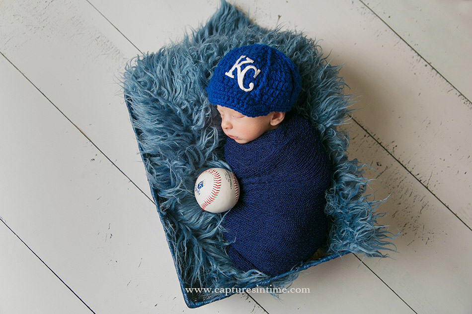 Kansas City Royals hat on newborn baby with game ball on blue fur rug