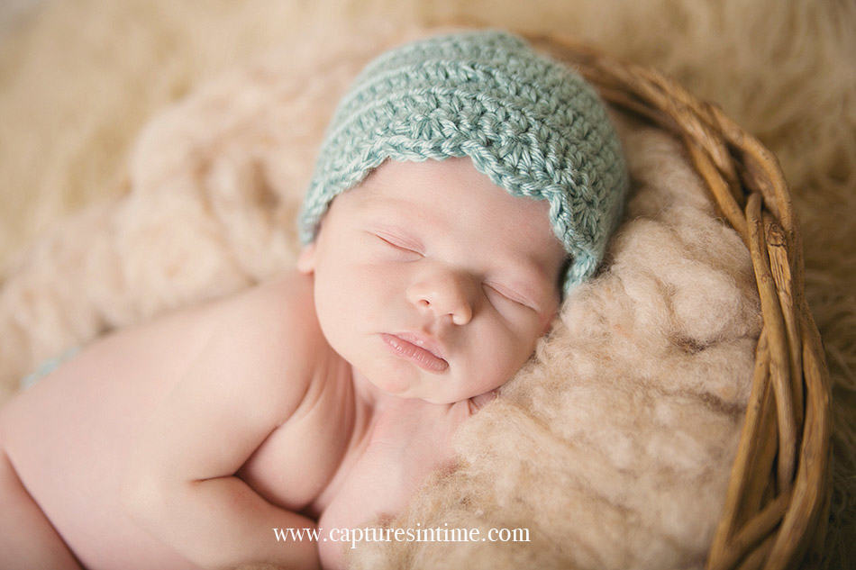 newborn boy laying on cream wool fluff with aqua hat on