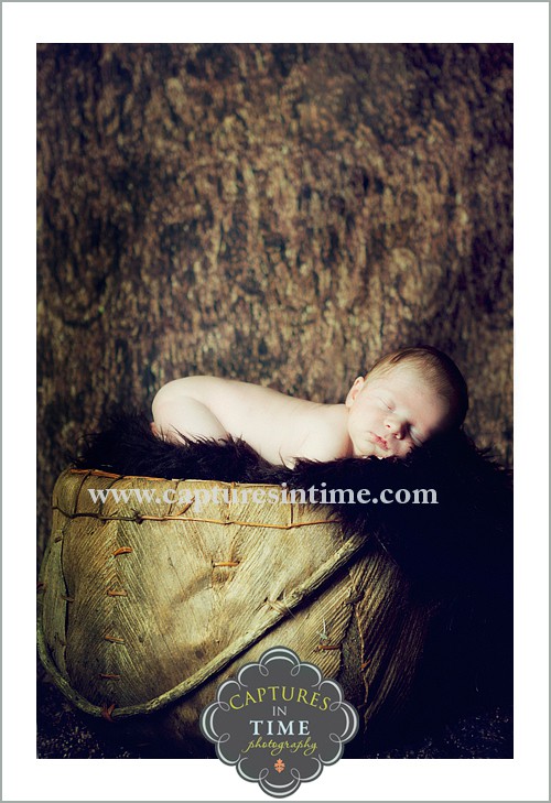 baby in dark brown rug and wooden basket on tummy
