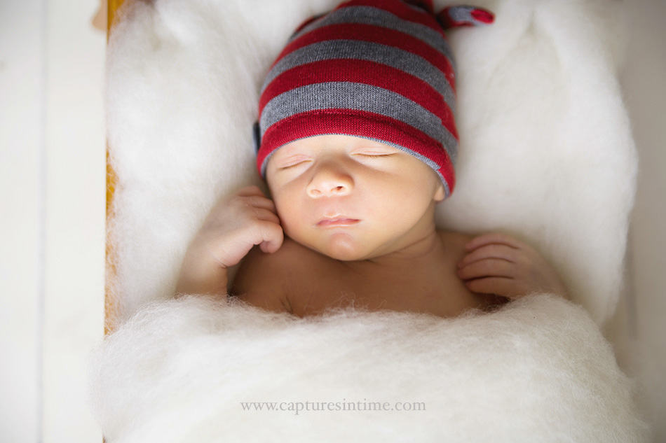 baby in red and grey hat on white fluff cloud