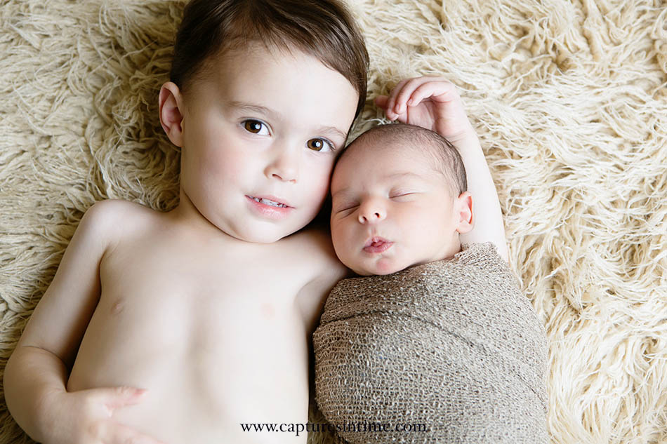 Sweet Newborn With Big Brother laying on fluffy cream rug