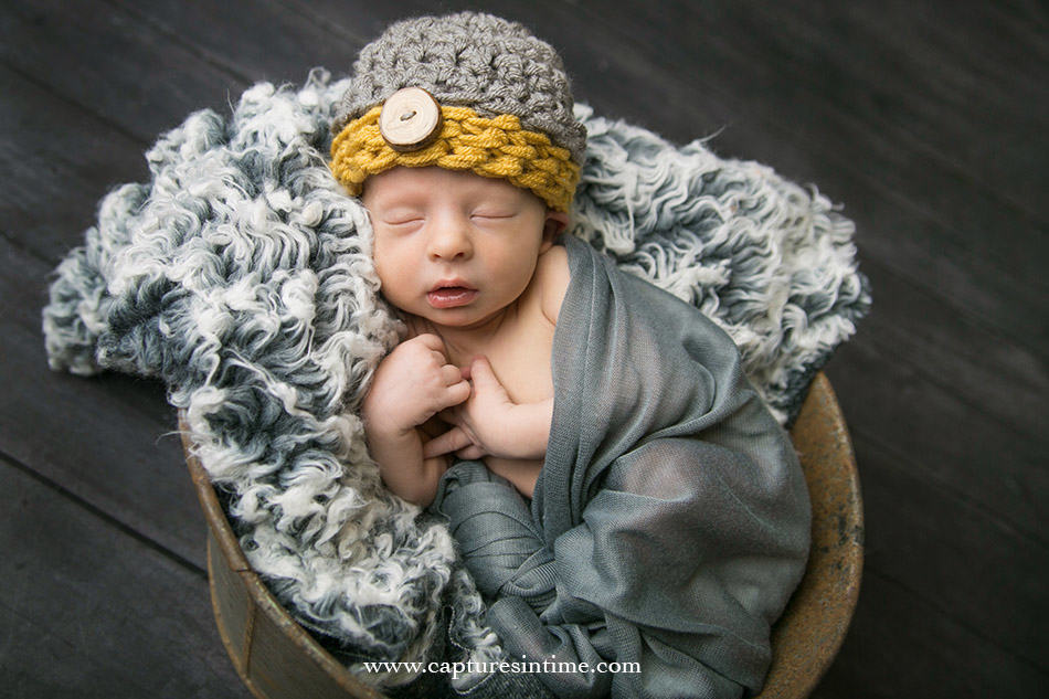 blonde newborn portrait on grey fur with grey and yellow hat