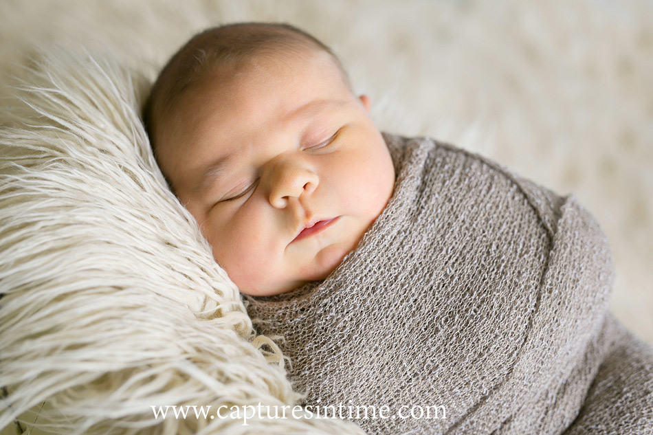 newborn baby boy swaddled laying on side on cream fur rug