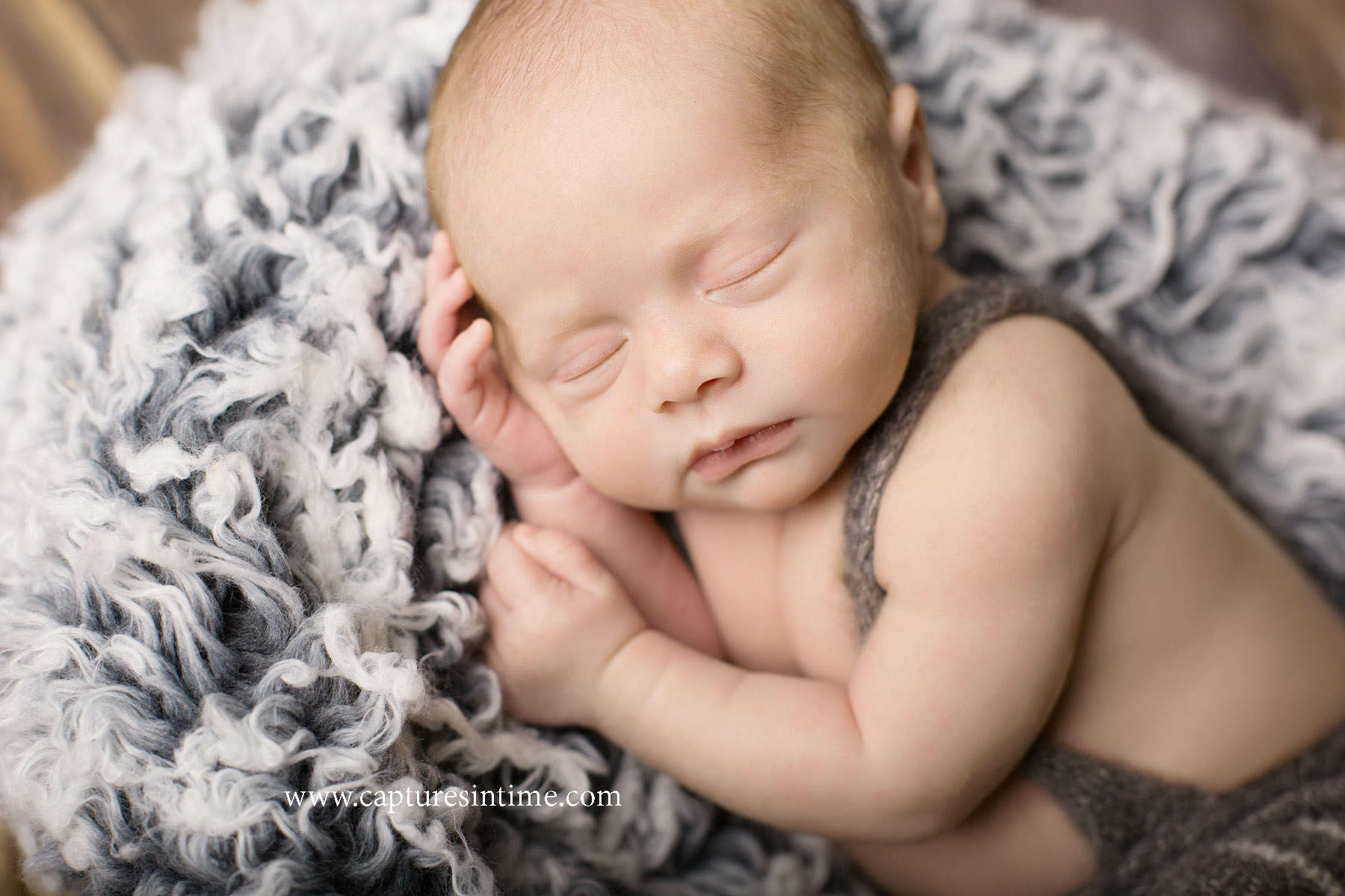 best kansas city newborn photos blonde newborn boy in suspender romper on curly gray blanket