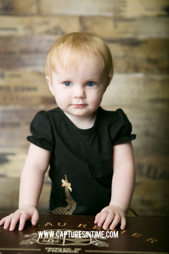 one year old girl black top standing in from of wood backdrop blue springs