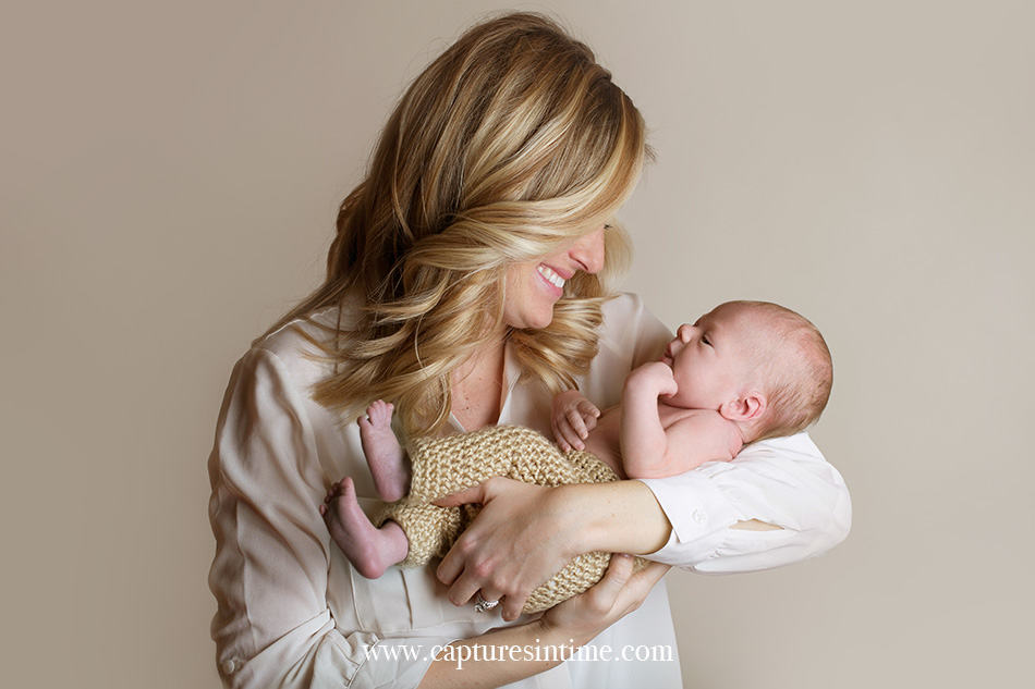 newborn photographer mom on cream backdrop holding her new baby boy smiling