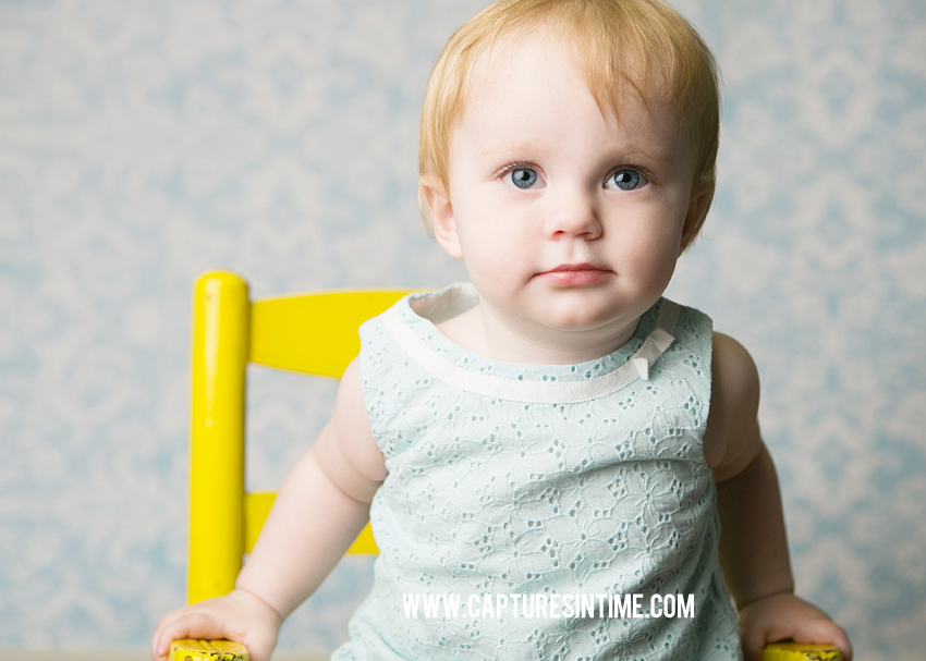 one year old girl blue top sitting in blue chair in front of blue backdrop blue springs