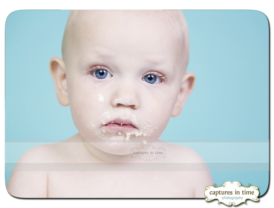 baby with cake on face in front of blue backdrop