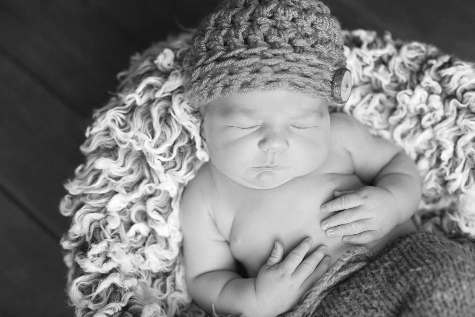 black and white image of baby with hat on fur rug