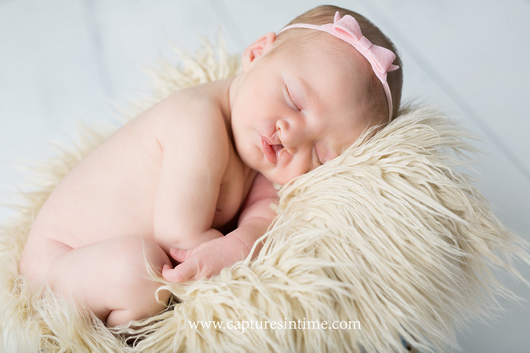 kansas city newborn baby photography newborn baby girl on wood floor with furry cream rug and pink bow in her hair